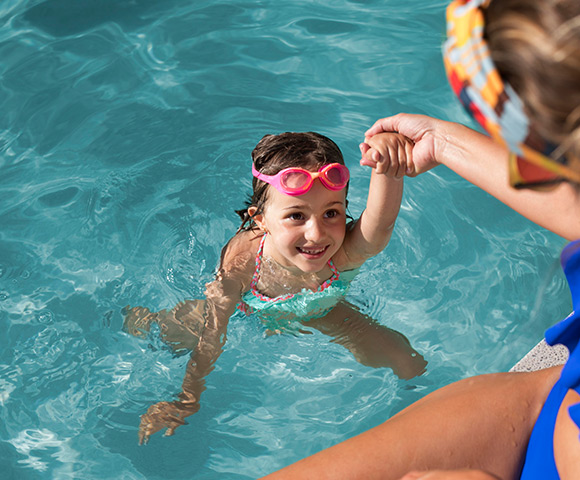 Imagem de criação nadando em piscina com ajuda de adulto. Confira como manter a piscina limpa por mais tempo.